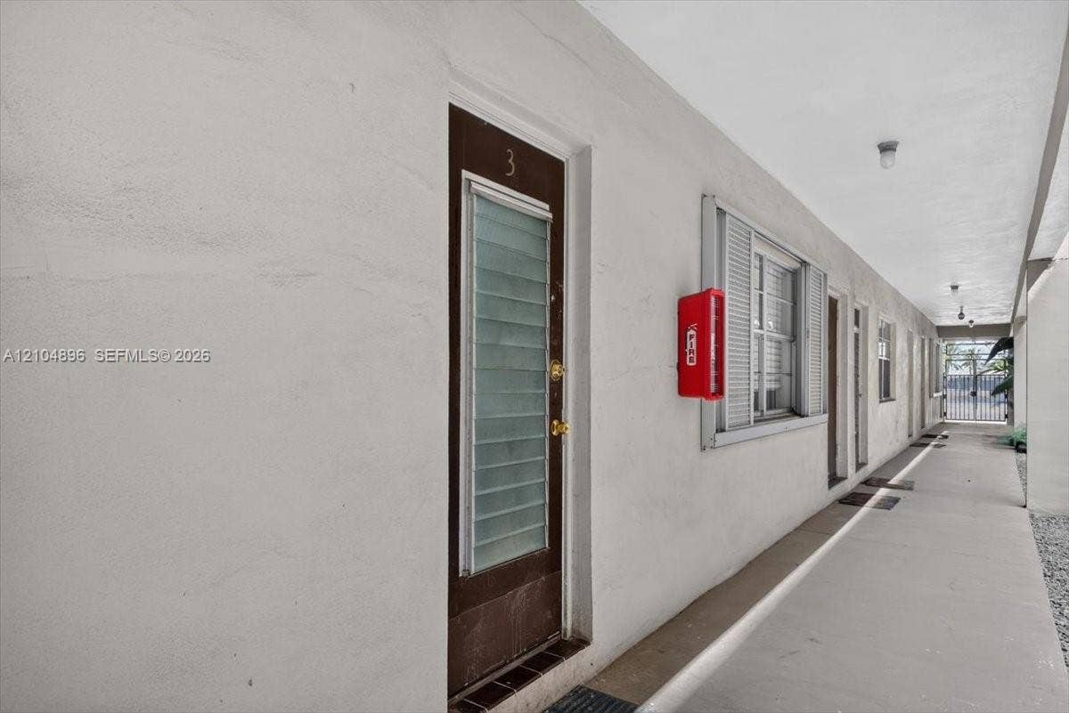 Exterior corridor featuring smooth-finish stucco walls, metal-frame doors with louvered glass inserts, and recessed ceiling lighting