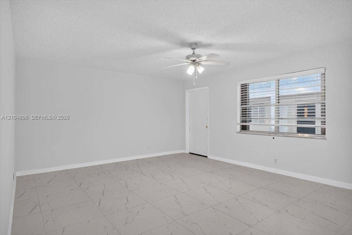 Interior space featuring large-format tile flooring with a neutral vein pattern, a ceiling fan with integrated light fixture, and a window with horizontal blinds