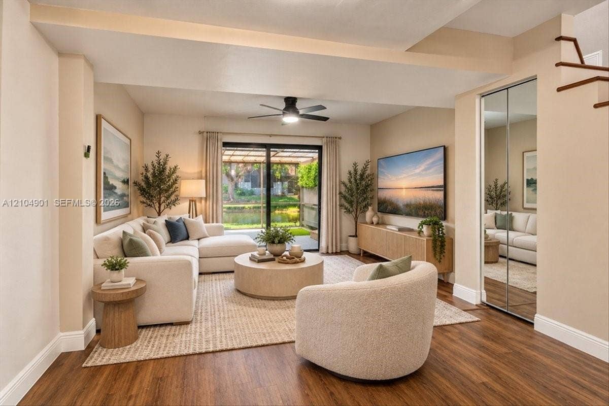 Living area featuring wood-finish flooring, sliding glass door access to an exterior patio, mirrored closet doors, and a ceiling fan