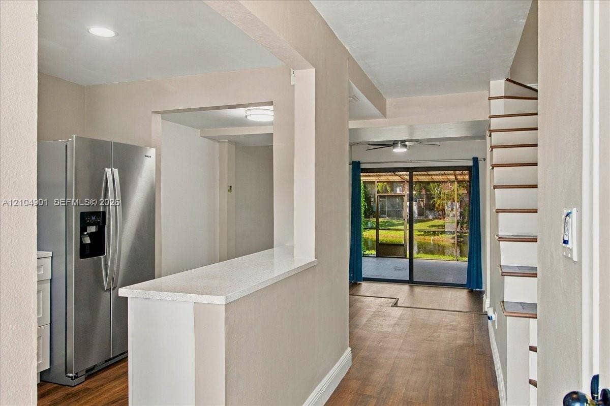 Kitchen area featuring a breakfast bar with stone-look countertop, stainless steel side-by-side refrigerator, wood-finish flooring, and floating staircase