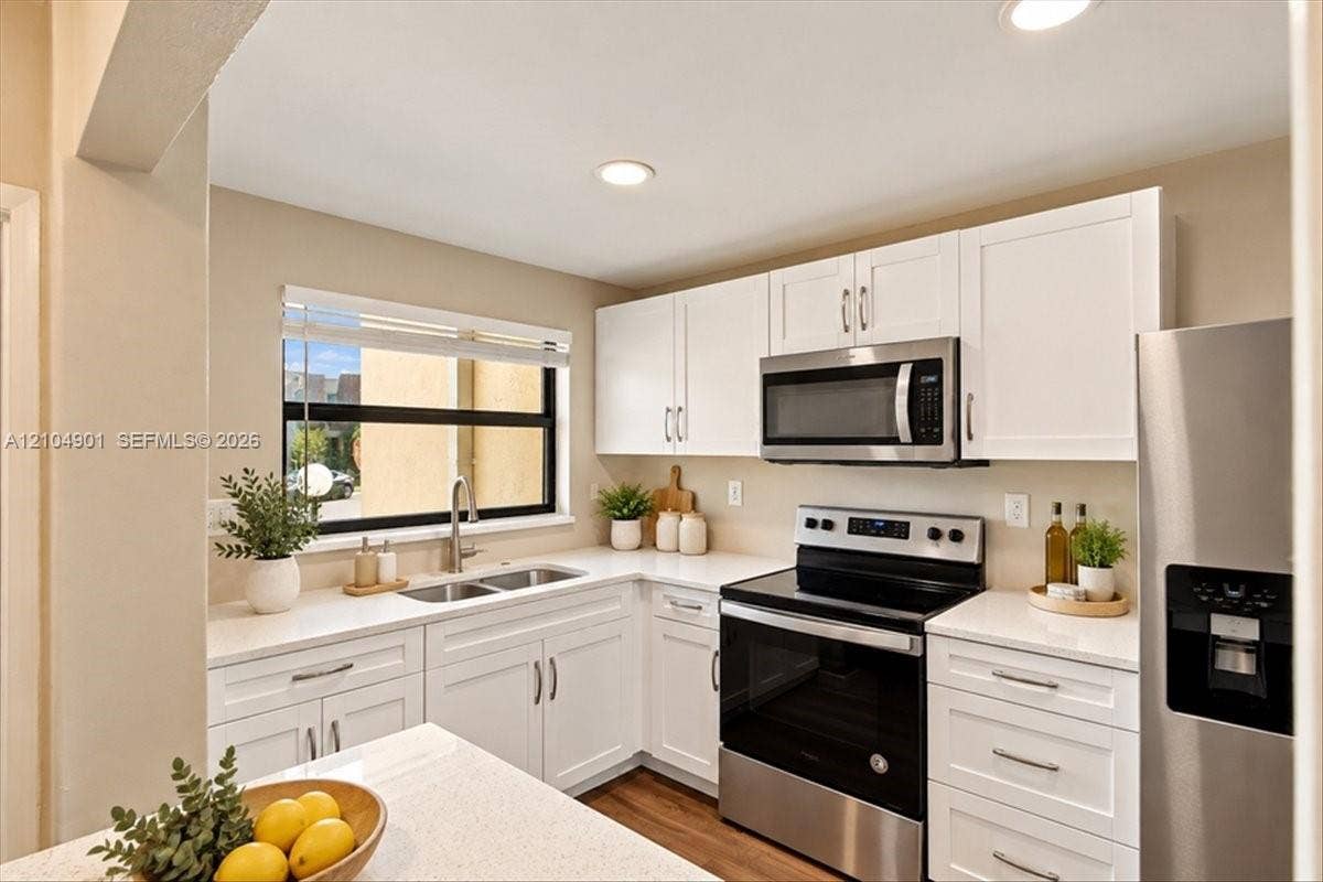 Kitchen featuring white shaker-style cabinetry, solid-surface countertops, recessed lighting, and stainless steel appliances