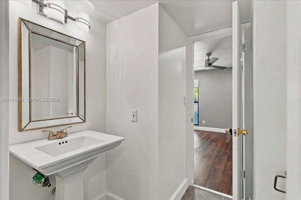 Pedestal sink with metallic faucet, wall-mounted beveled-edge mirror, and multi-light vanity fixture