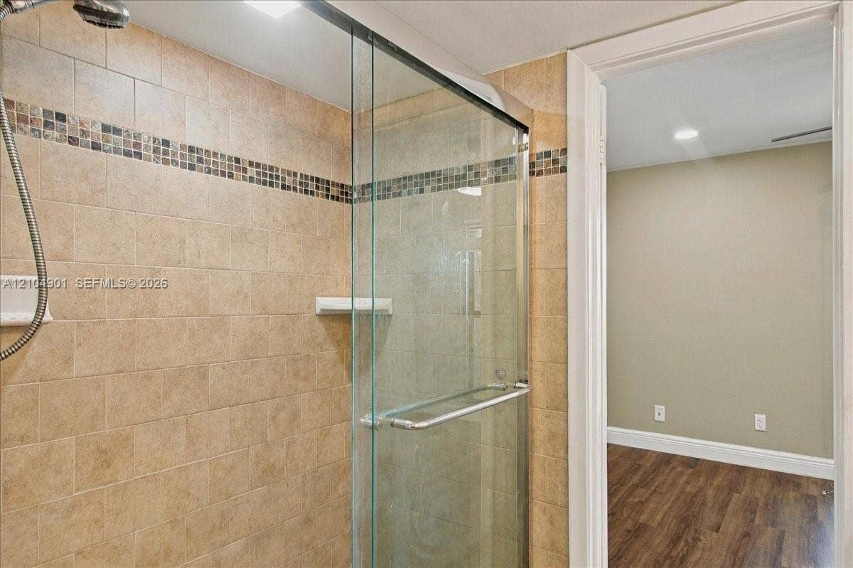 Walk-in shower featuring glass enclosure, wall-mounted shower head, mosaic tile accent border, and ceramic tile surround