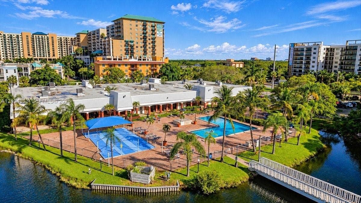 501 E Dania Beach Boulevard, #5-4A, Dania, Dania Beach, FL 33004 Recreational area featuring a swimming pool, a multi-use sports court with a canopy cover, brick paver decking, and a pedestrian bridge over the water
