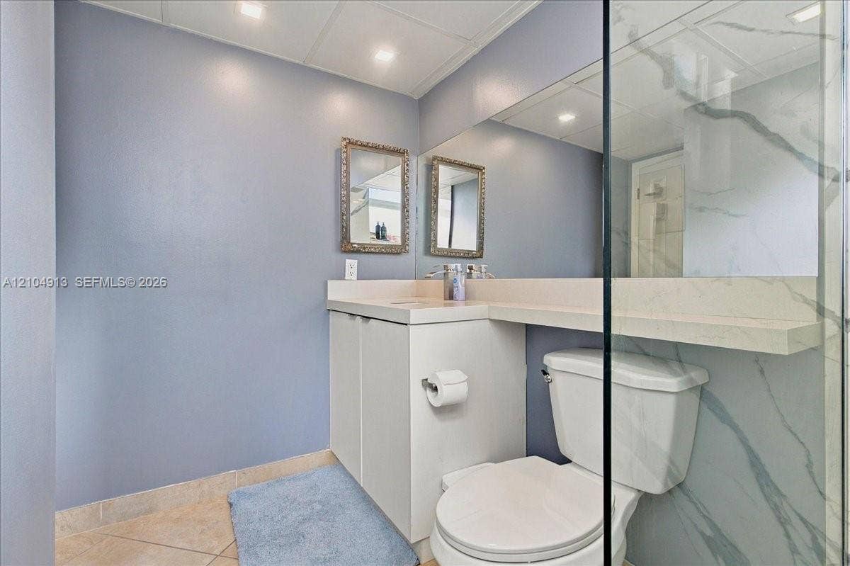 501 E Dania Beach Boulevard, #5-4A, Dania, Dania Beach, FL 33004 Built-in vanity featuring a light-toned countertop, large wall-mounted mirror, glass-enclosed shower with stone-finish surround, and tile flooring