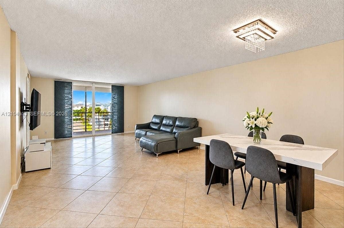 501 E Dania Beach Boulevard, #5-4A, Dania, Dania Beach, FL 33004 Open-concept living space featuring ceramic tile flooring, a tiered crystal flush-mount light fixture, and floor-to-ceiling sliding glass doors opening to an exterior balcony