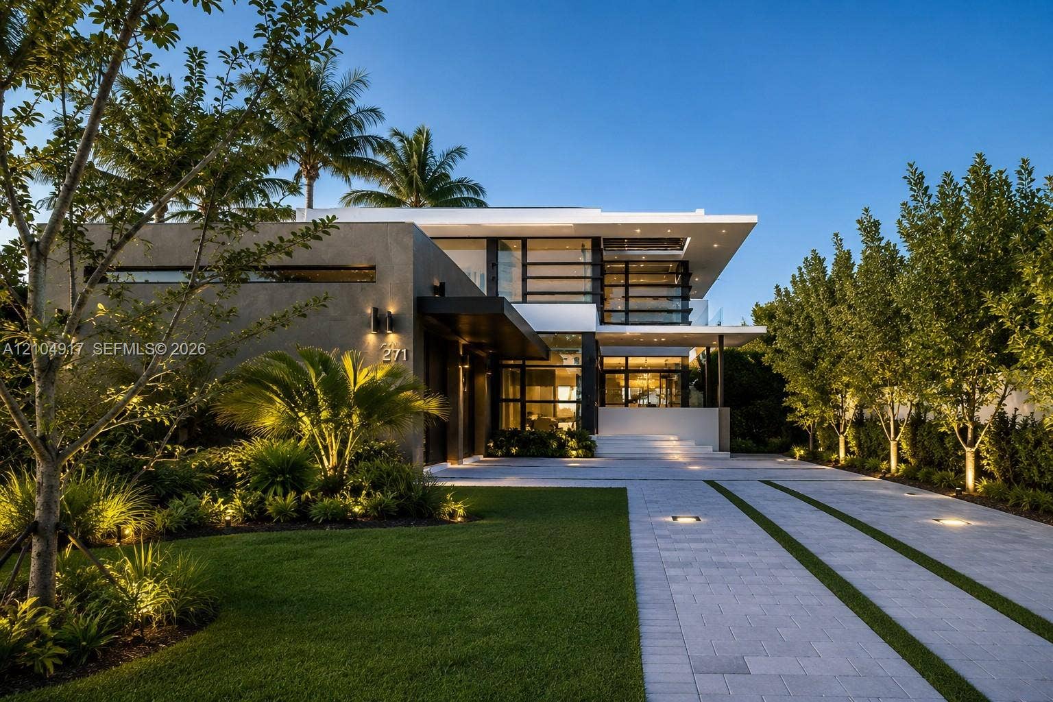 Modern two-story architectural exterior featuring smooth stucco finish, expansive glass windows, integrated landscape lighting, and a paved driveway with linear grass accents