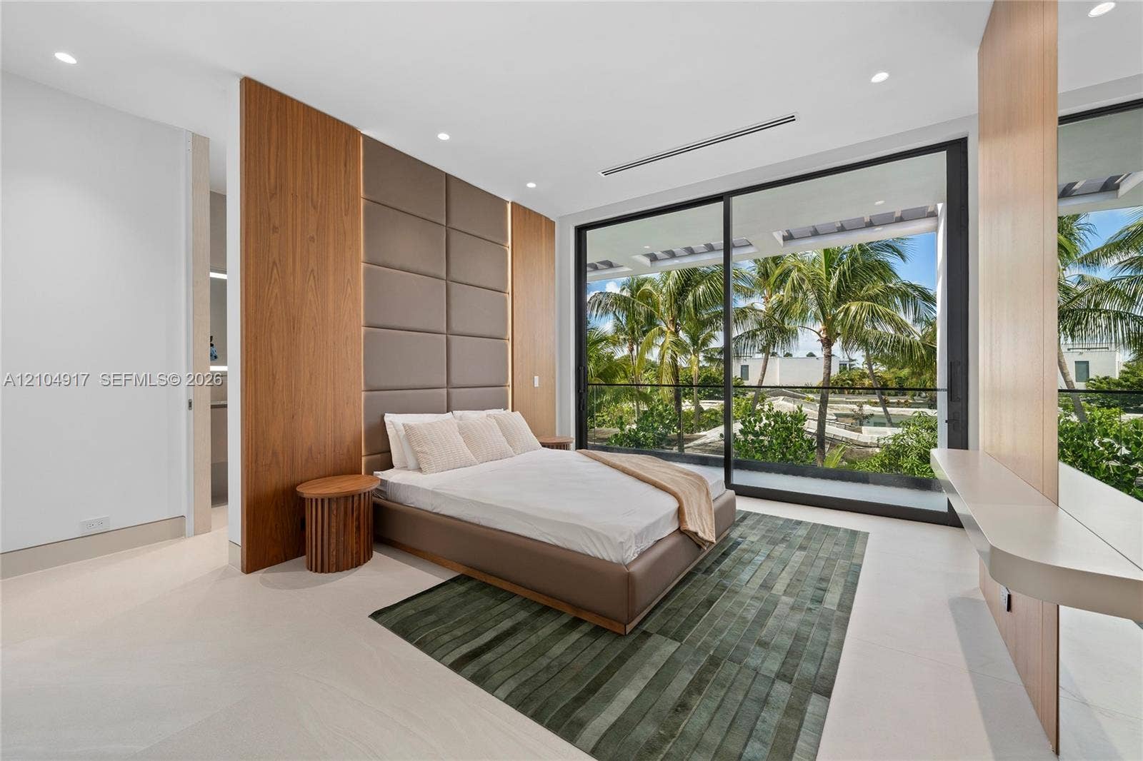 Full-height sliding glass doors, recessed lighting, a built-in wall panel headboard, wood-finish accent walls, and light-toned flooring