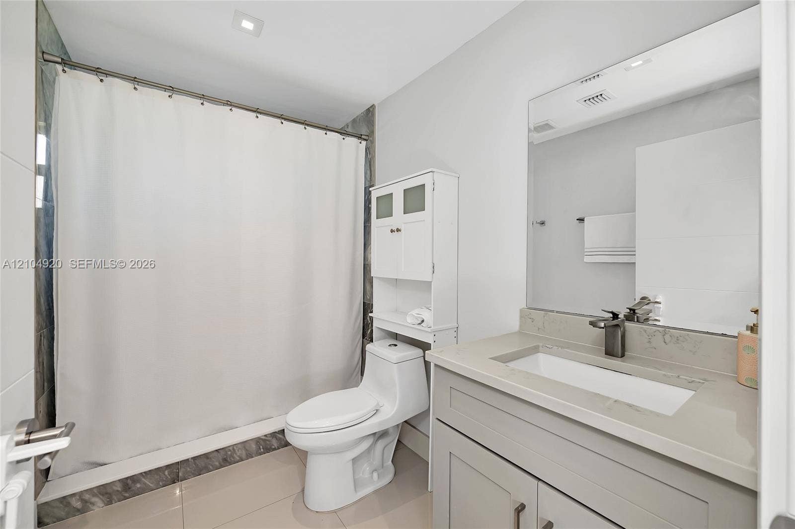 Bathroom featuring a stone-surface vanity with an integrated rectangular sink, wall-spanning mirror, one-piece toilet, and tile shower surround