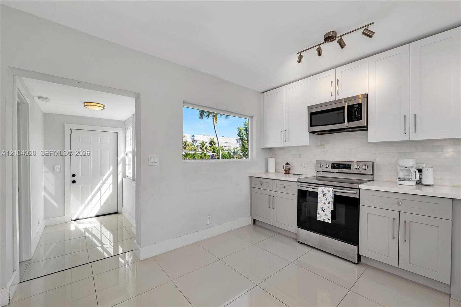 Kitchen featuring white and grey shaker-style cabinetry, stainless steel appliances, polished stone-finish tile flooring, and track lighting