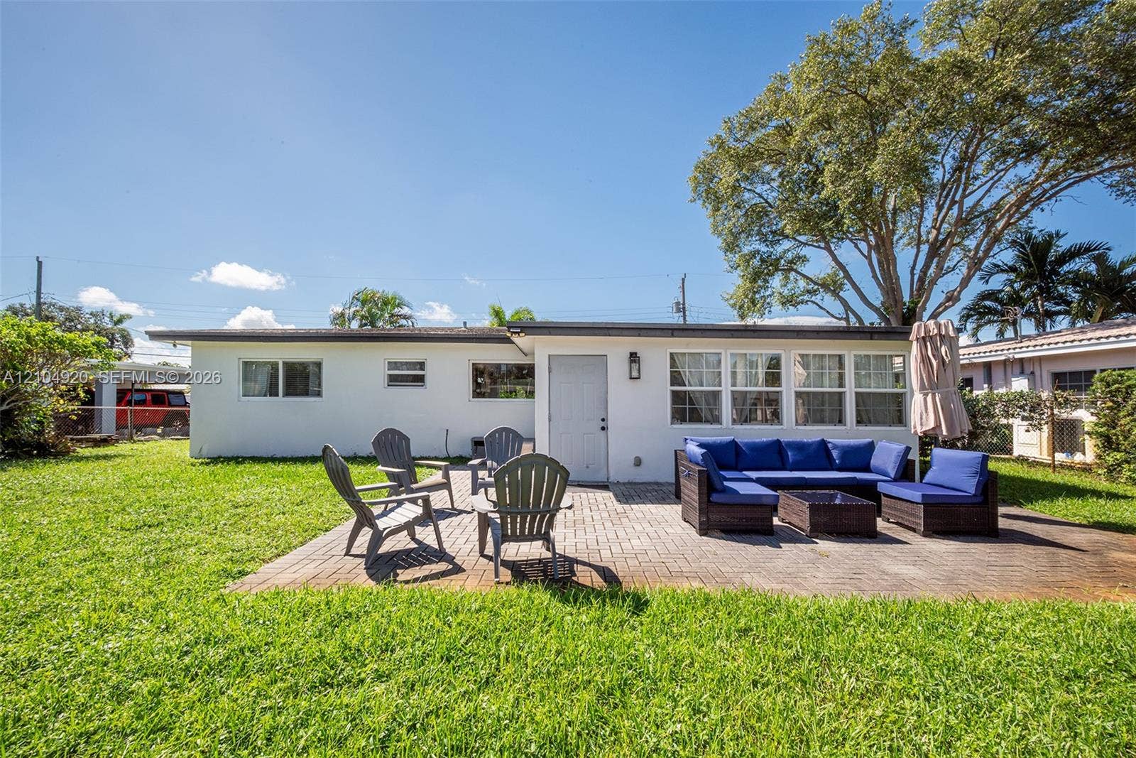 Rear exterior featuring a paver patio, mature trees, and a level lawn area