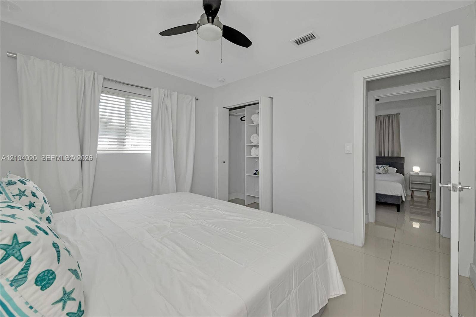 Neutral-toned interior featuring oversized tile flooring, a ceiling fan with integrated lighting, a built-in closet shelving system, and horizontal window blinds