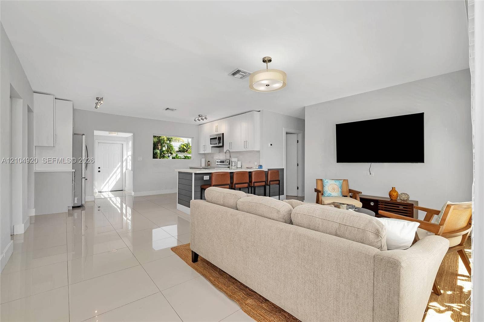 Open-concept interior featuring large-format polished tile flooring, white cabinetry, kitchen island with dark paneling, recessed lighting, and contemporary semi-flush mount light fixtures