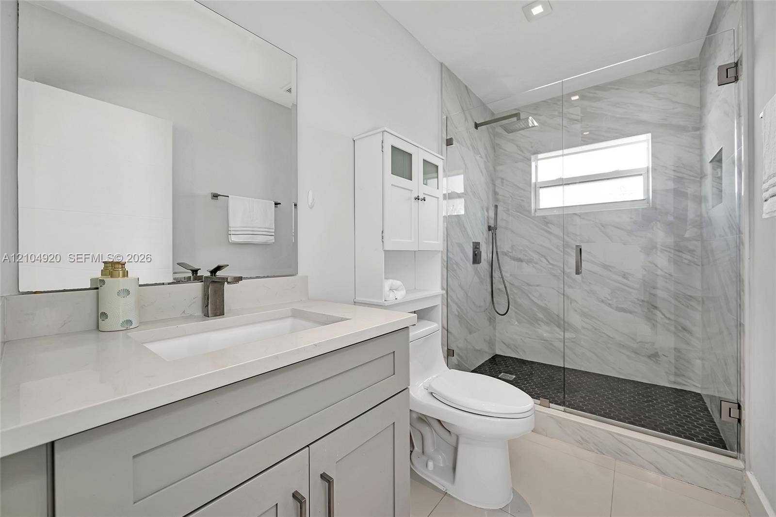 Bathroom featuring a grey vanity with a rectangular sink, stone-finish countertop, walk-in shower with floor-to-ceiling tile, and a wall-mounted glass enclosure