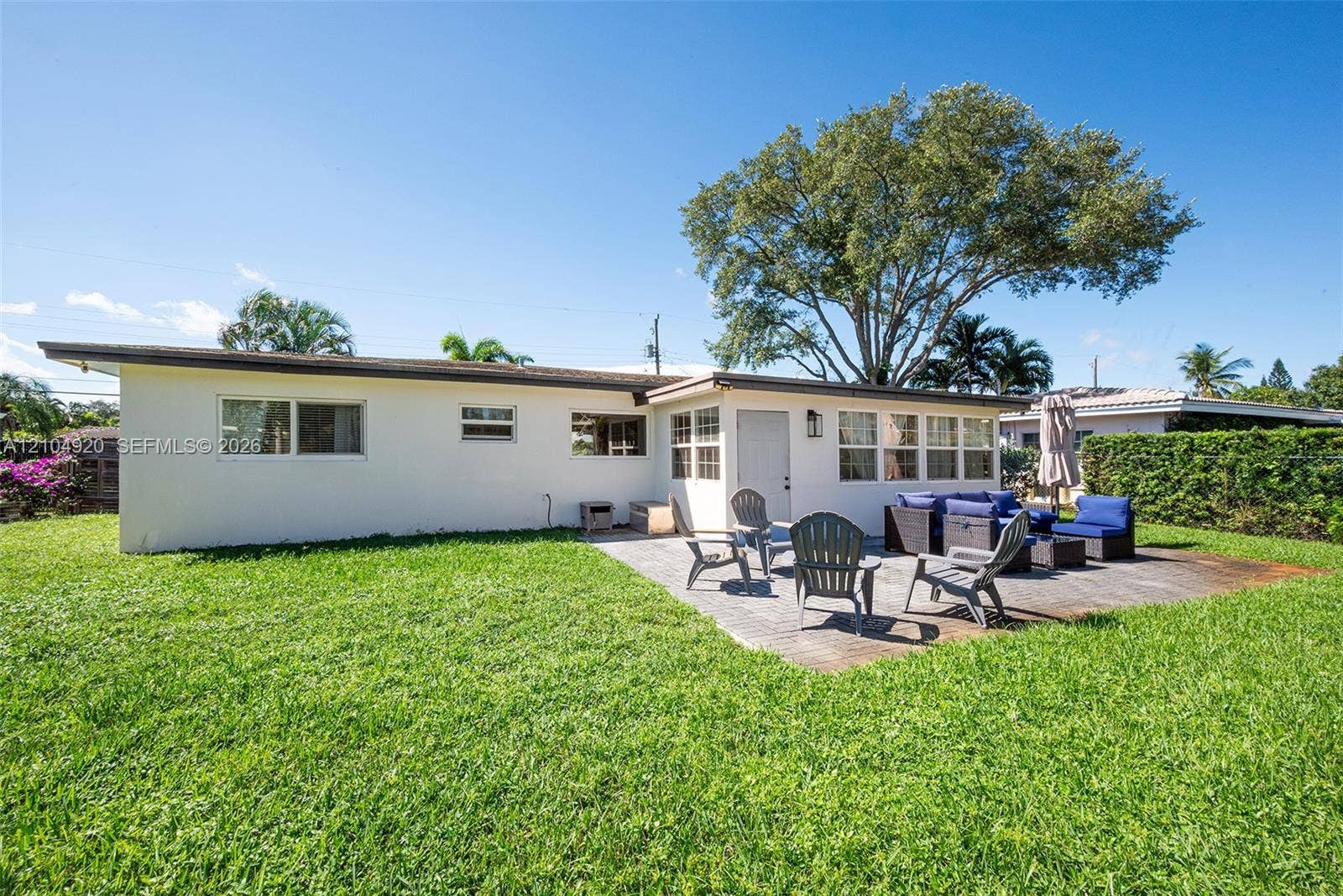 Backyard featuring a paved patio, expansive lawn, perimeter hedge, and mature trees