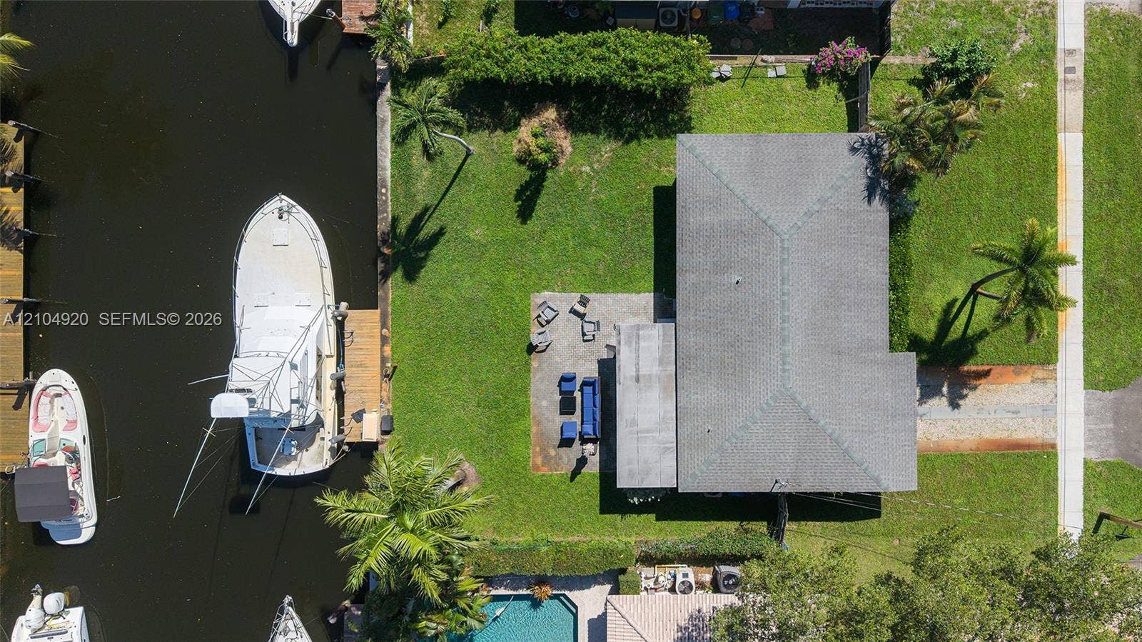 Waterfront lot featuring a private boat dock, concrete patio, expansive lawn, and mature palm trees
