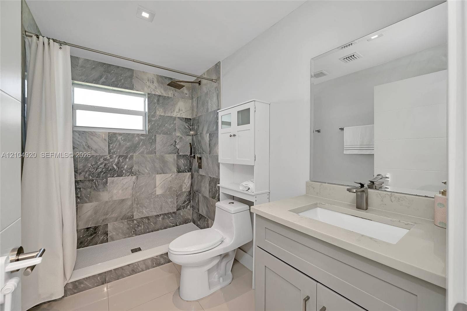 Full-height shower enclosure featuring stone-tiled walls and an overhead rain showerhead, complemented by a stone-topped vanity with an integrated basin and polished metal fixtures
