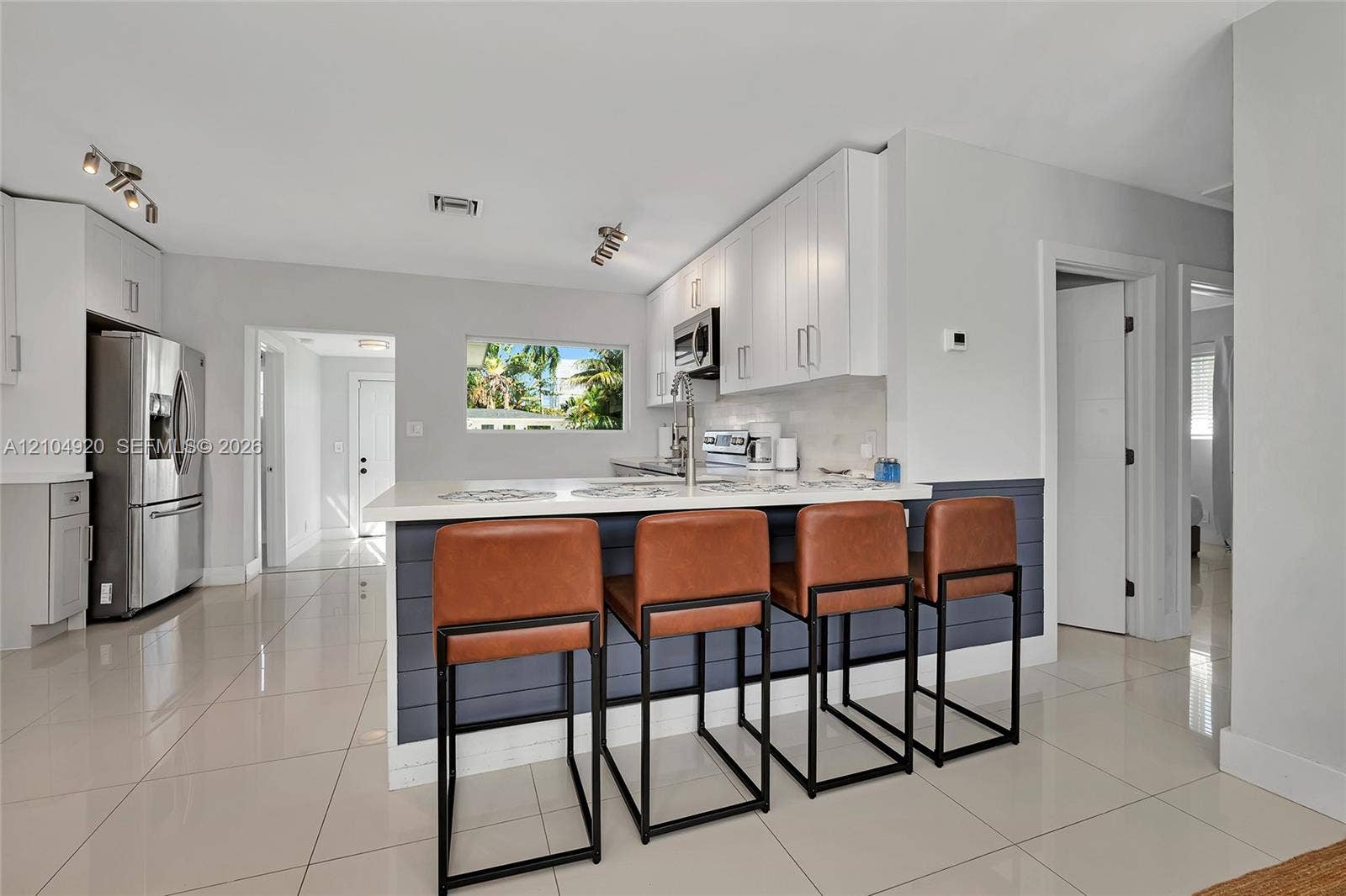 Kitchen featuring white cabinetry, quartz countertops, a shiplap-accented breakfast bar, polished tile flooring, and stainless steel appliances