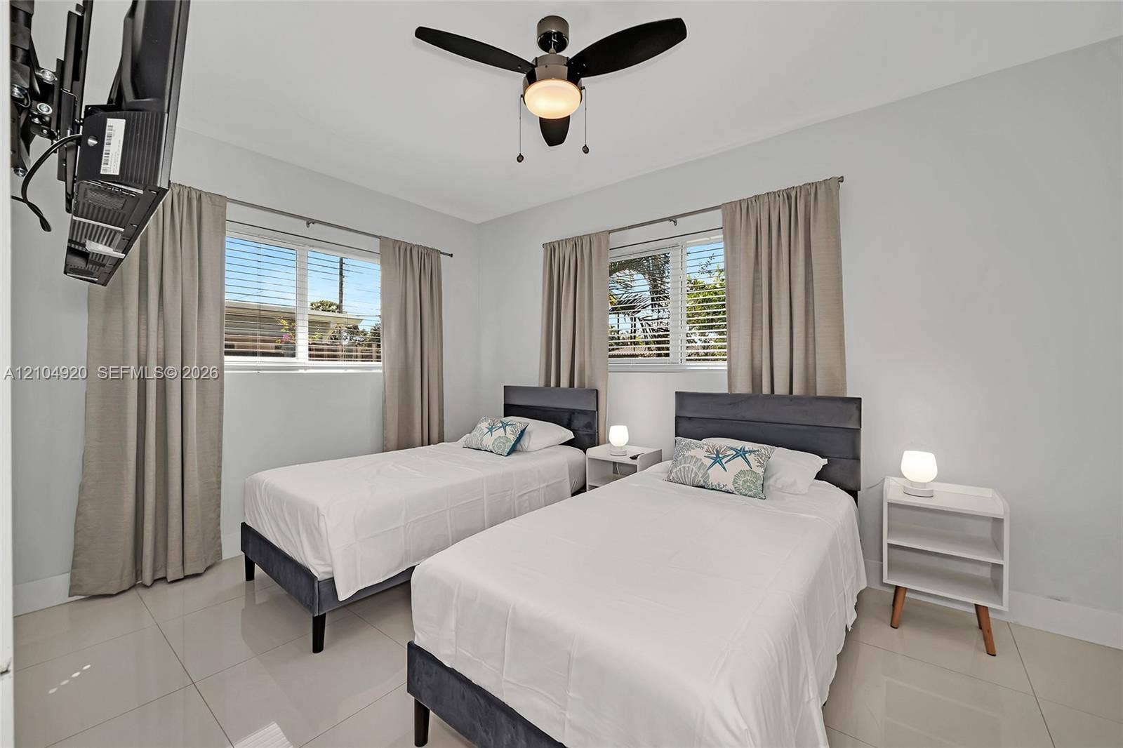 Neutral-toned interior space featuring light-colored tile flooring, multiple windows with horizontal blinds, and a contemporary ceiling fan with integrated lighting