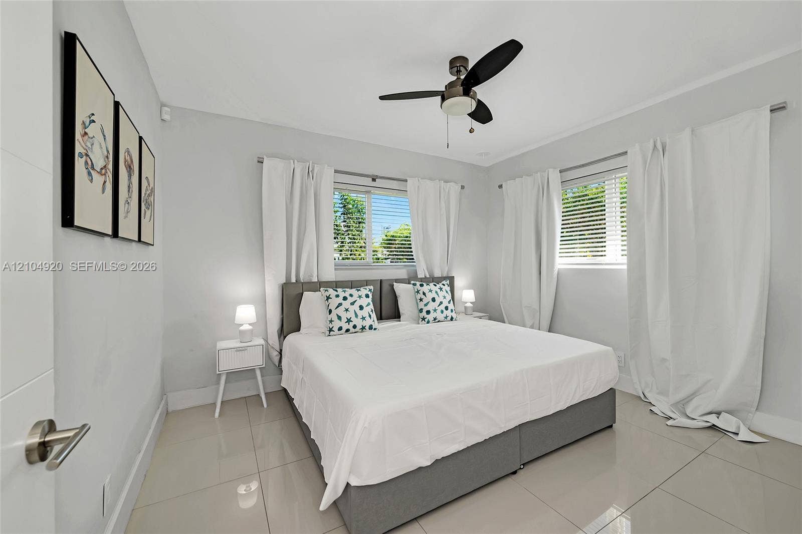 Neutral-toned interior featuring large-format tile flooring, multi-pane windows with horizontal blinds, and a central ceiling fan with integrated light fixture