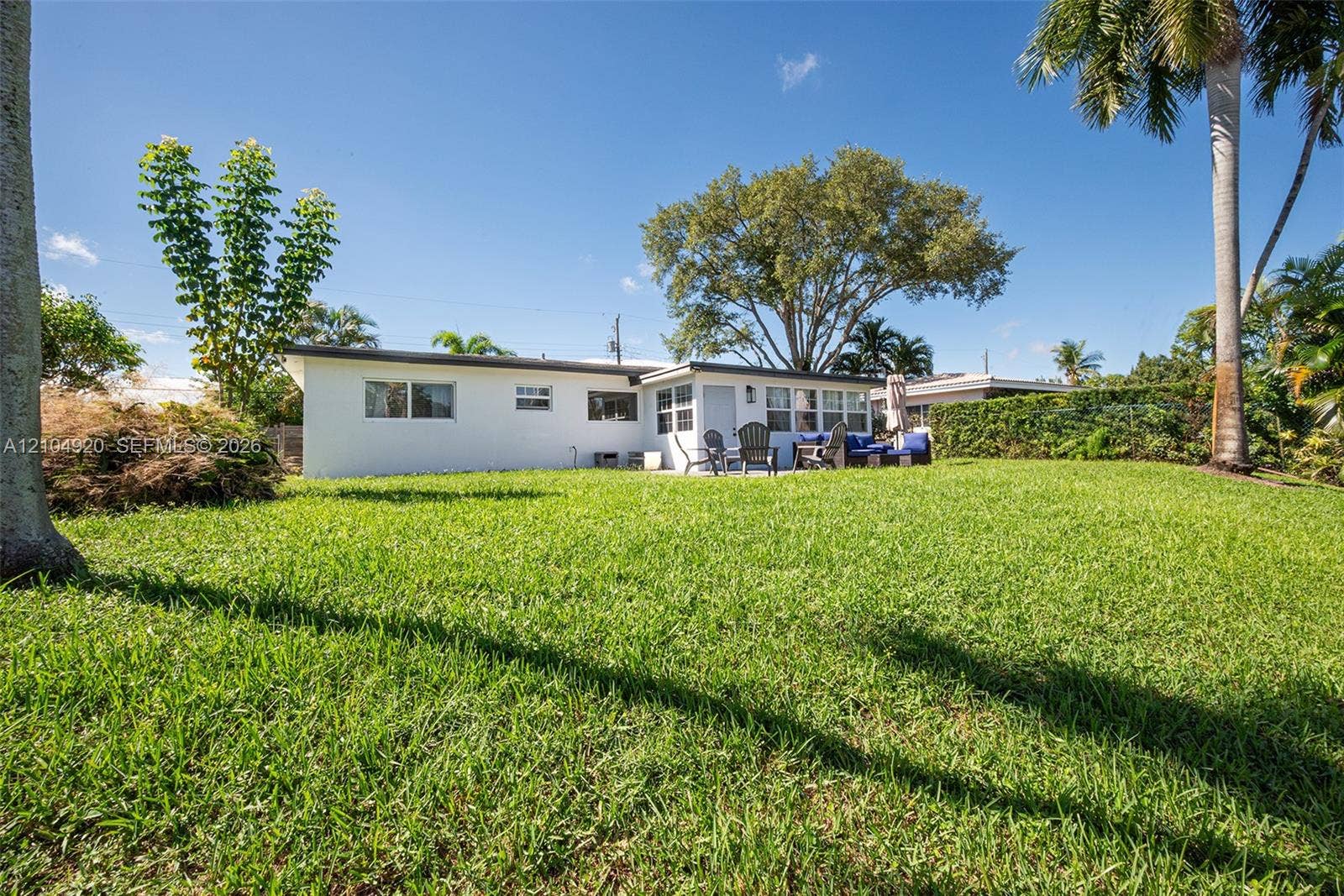 Expansive backyard featuring a sprawling grass lawn, mature trees, and a white exterior residence with a concrete patio