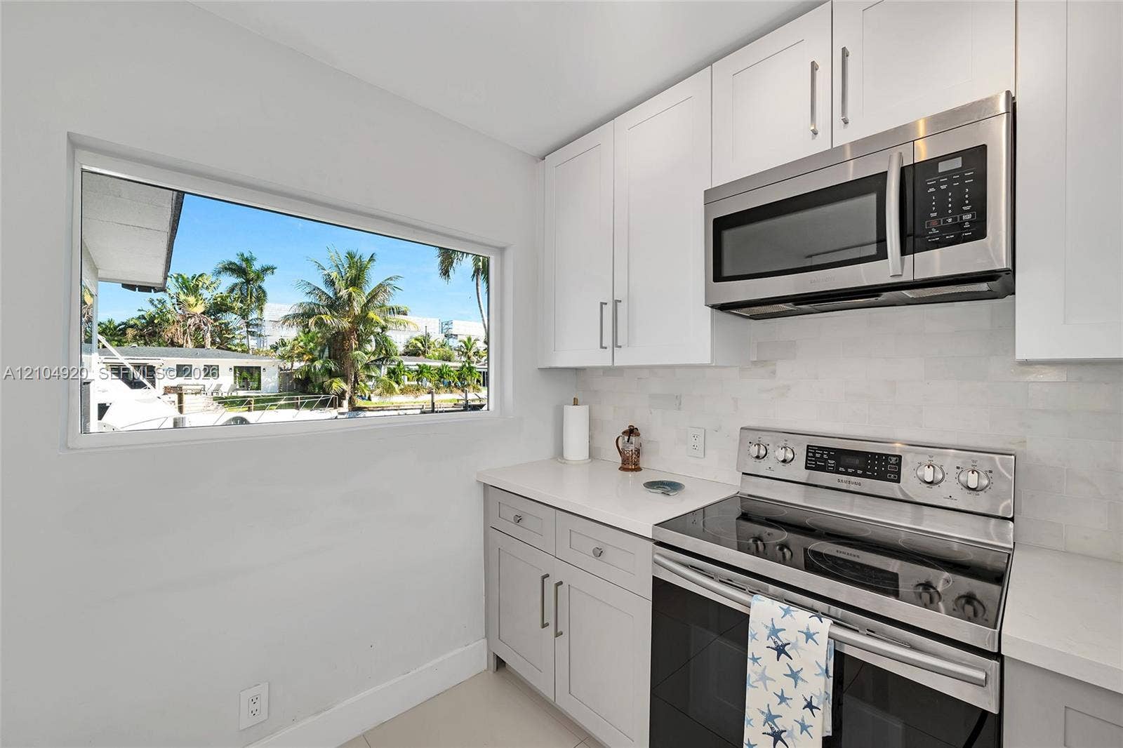 Kitchen featuring shaker-style cabinetry, stainless steel microwave, glass-top range, solid surface countertops, and white subway tile backsplash