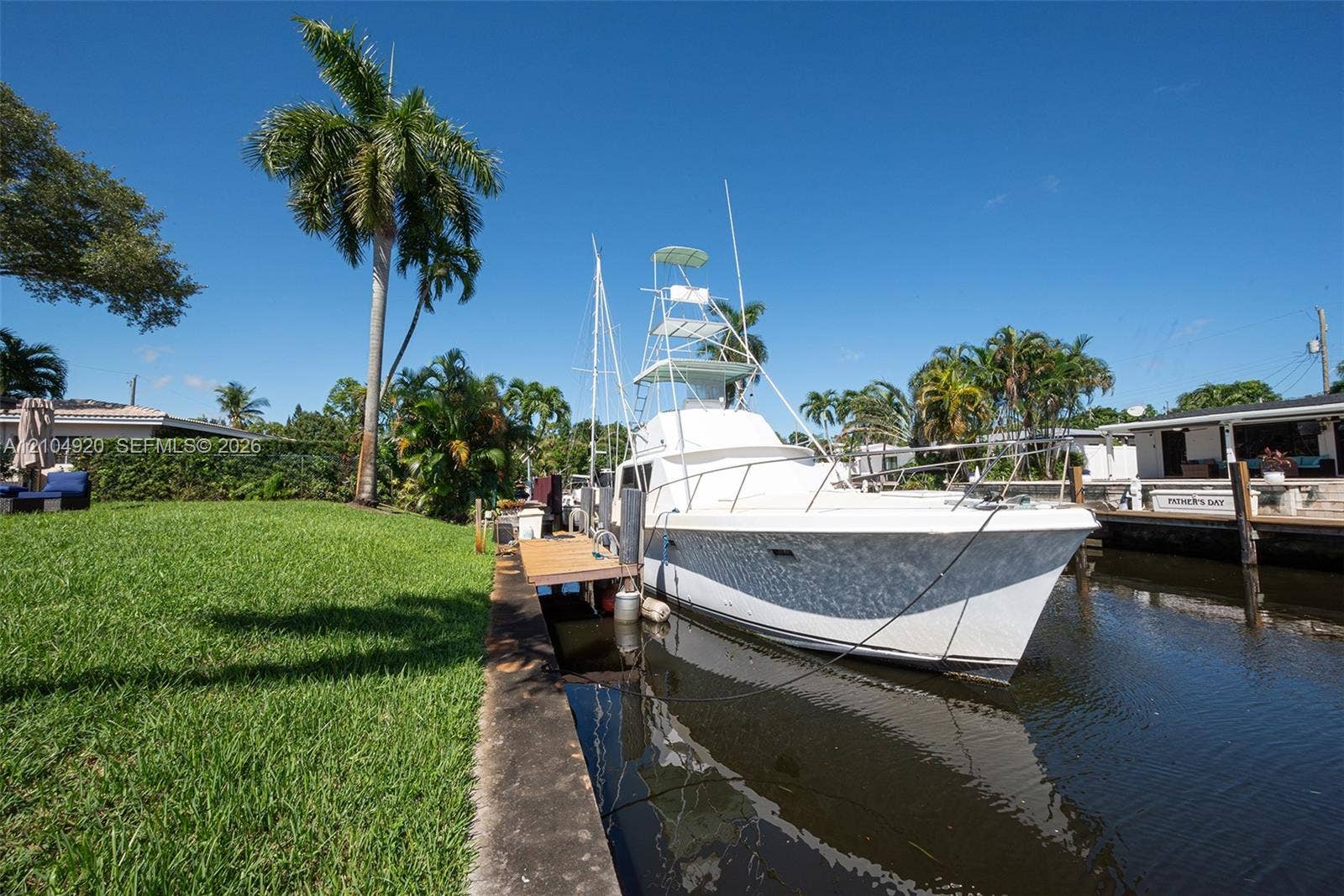 Waterfront property featuring a private boat slip, concrete seawall, and expansive grass lawn with mature palm trees
