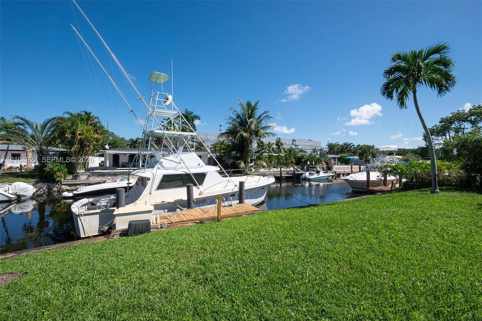 Waterfront property featuring a private wooden dock, bulkhead sea wall, manicured lawn, and mature palm trees