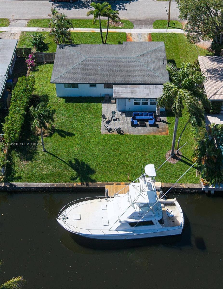 Waterfront property featuring a private dock, concrete patio, expansive lawn, and mature palm trees