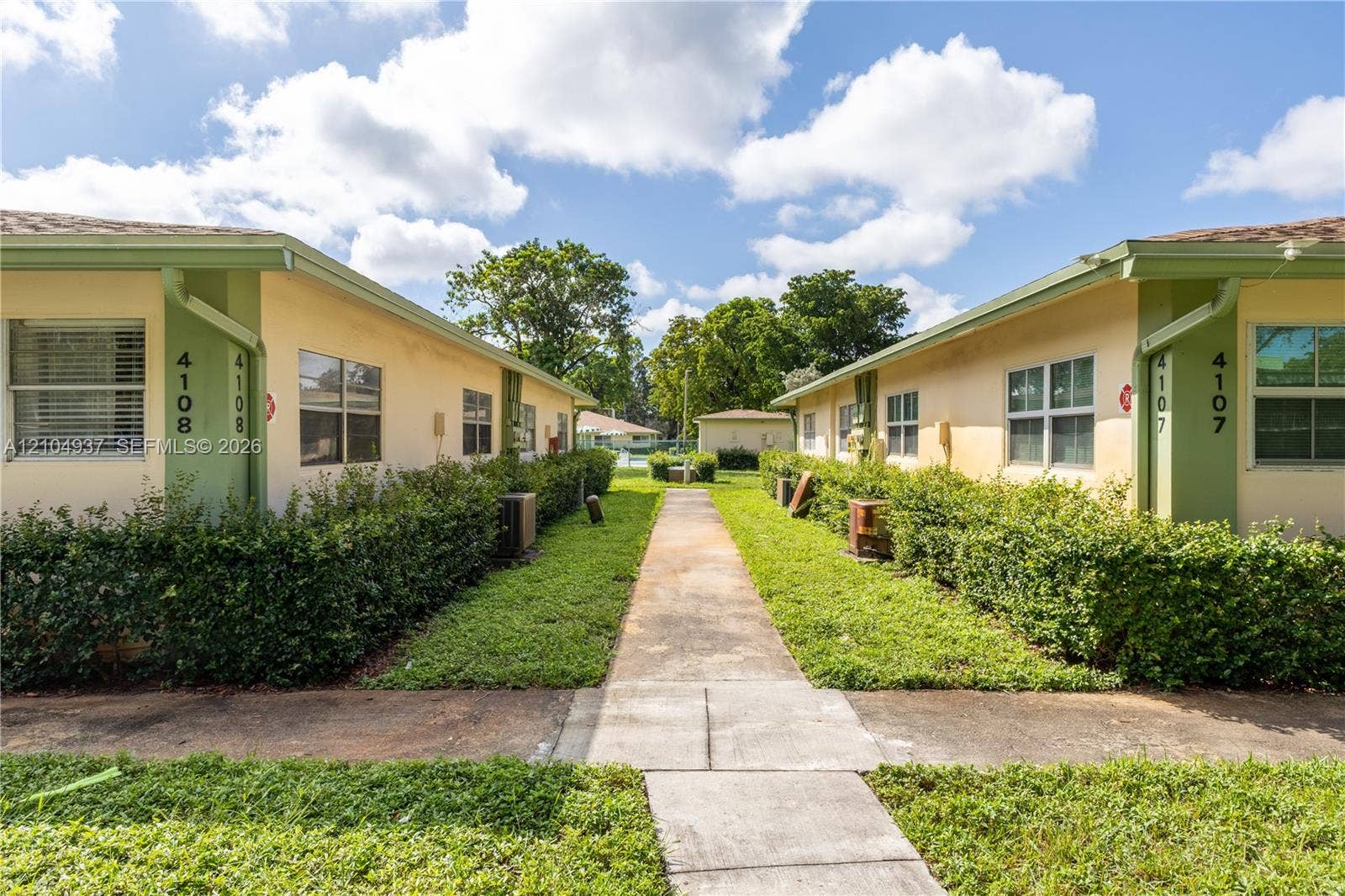 4108 NW 88th Avenue, #3, Coral Springs, FL 33065 Exterior view of stucco buildings featuring a concrete walkway, trimmed shrubbery, and multi-pane horizontal windows