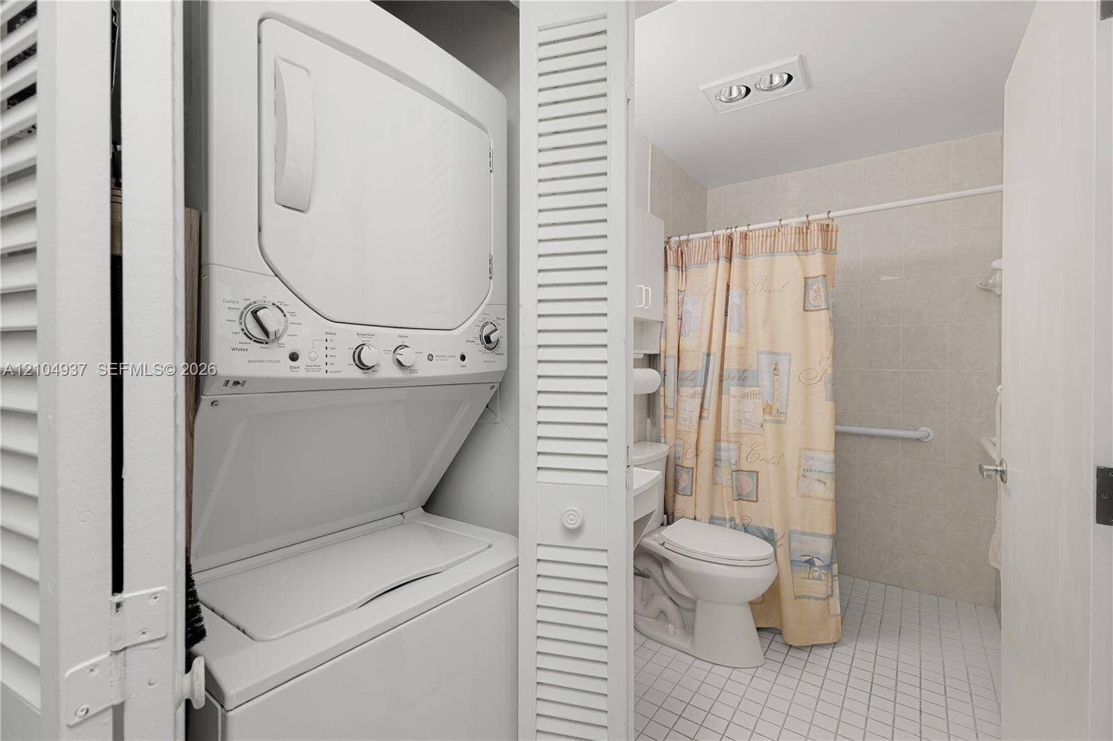 4108 NW 88th Avenue, #3, Coral Springs, FL 33065 Stacked laundry unit housed in a louvered closet, bathroom featuring a tiled shower enclosure, white porcelain toilet, and grid-patterned floor tile