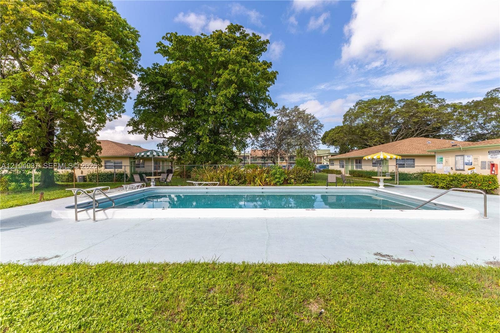 4108 NW 88th Avenue, #3, Coral Springs, FL 33065 Rectangular in-ground swimming pool featuring a concrete pool deck, stainless steel entry rails, chain-link perimeter fencing, and mature landscaping