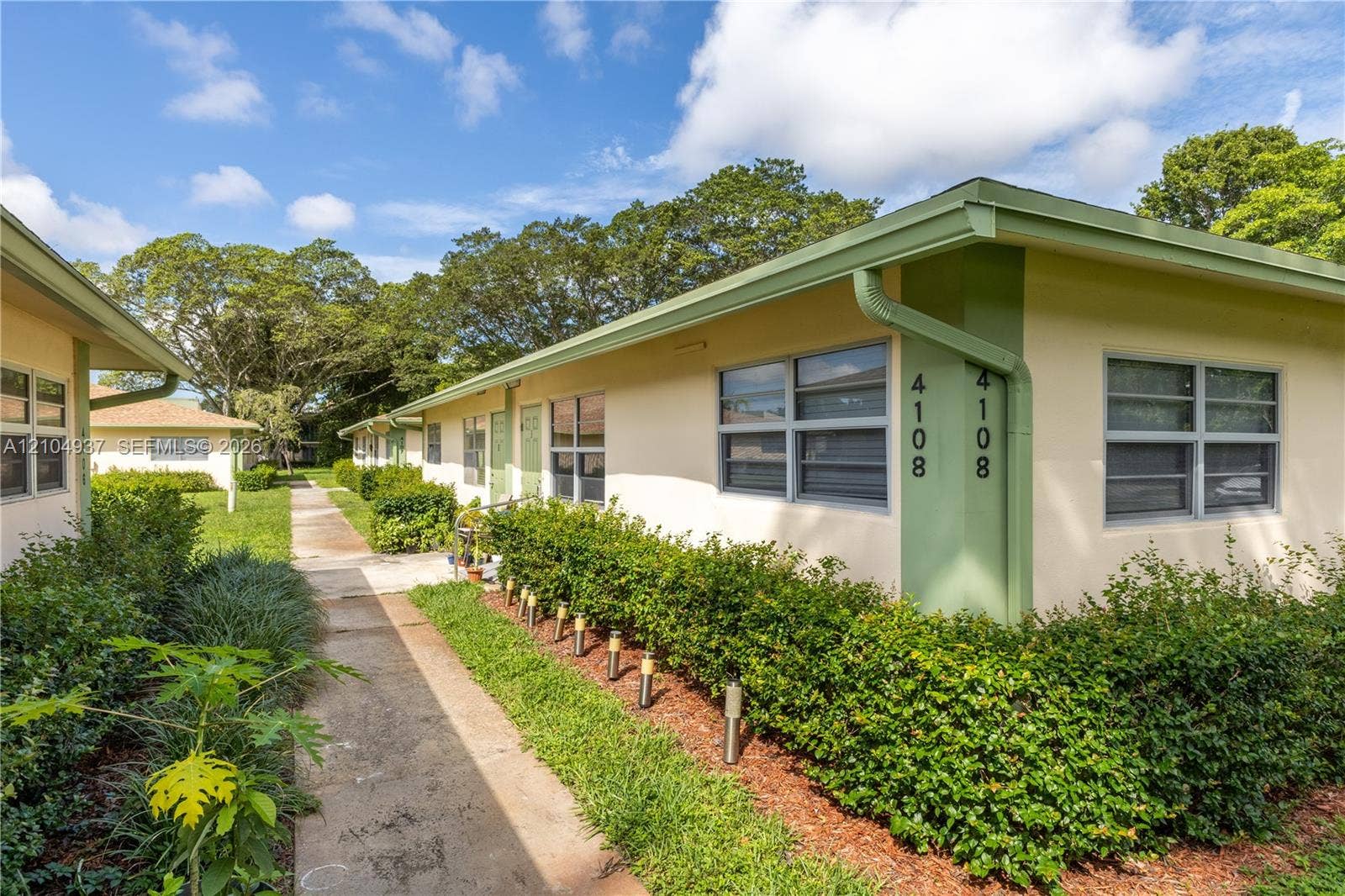 4108 NW 88th Avenue, #3, Coral Springs, FL 33065 Single-story exterior featuring light-toned stucco siding, horizontal sliding windows, concrete walkways, and established landscape hedging