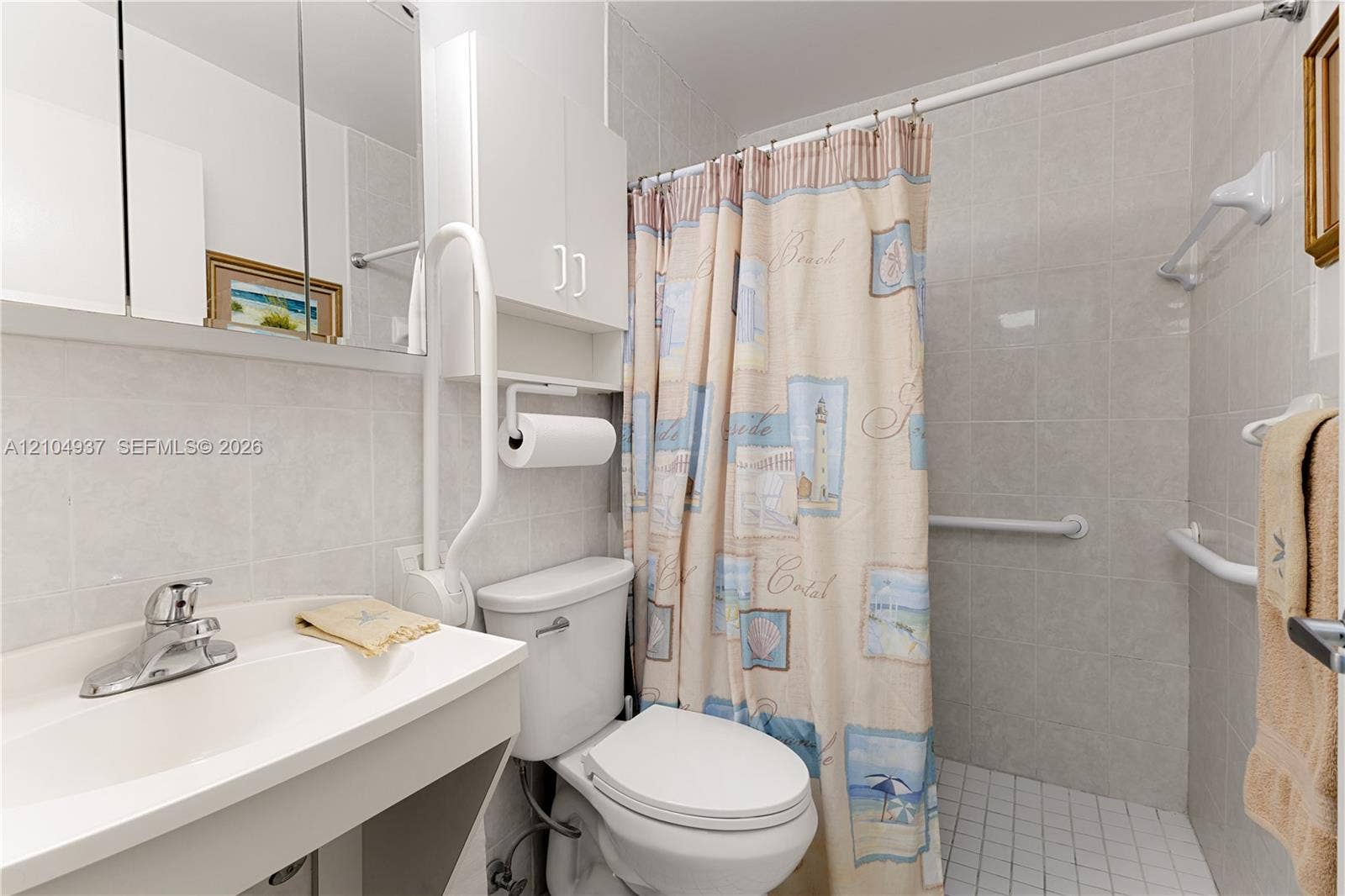 4108 NW 88th Avenue, #3, Coral Springs, FL 33065 Bathroom featuring floor-to-ceiling tile, white vanity with an integrated basin, mirrored medicine cabinet, built-in upper wall storage, and wall-mounted support bars