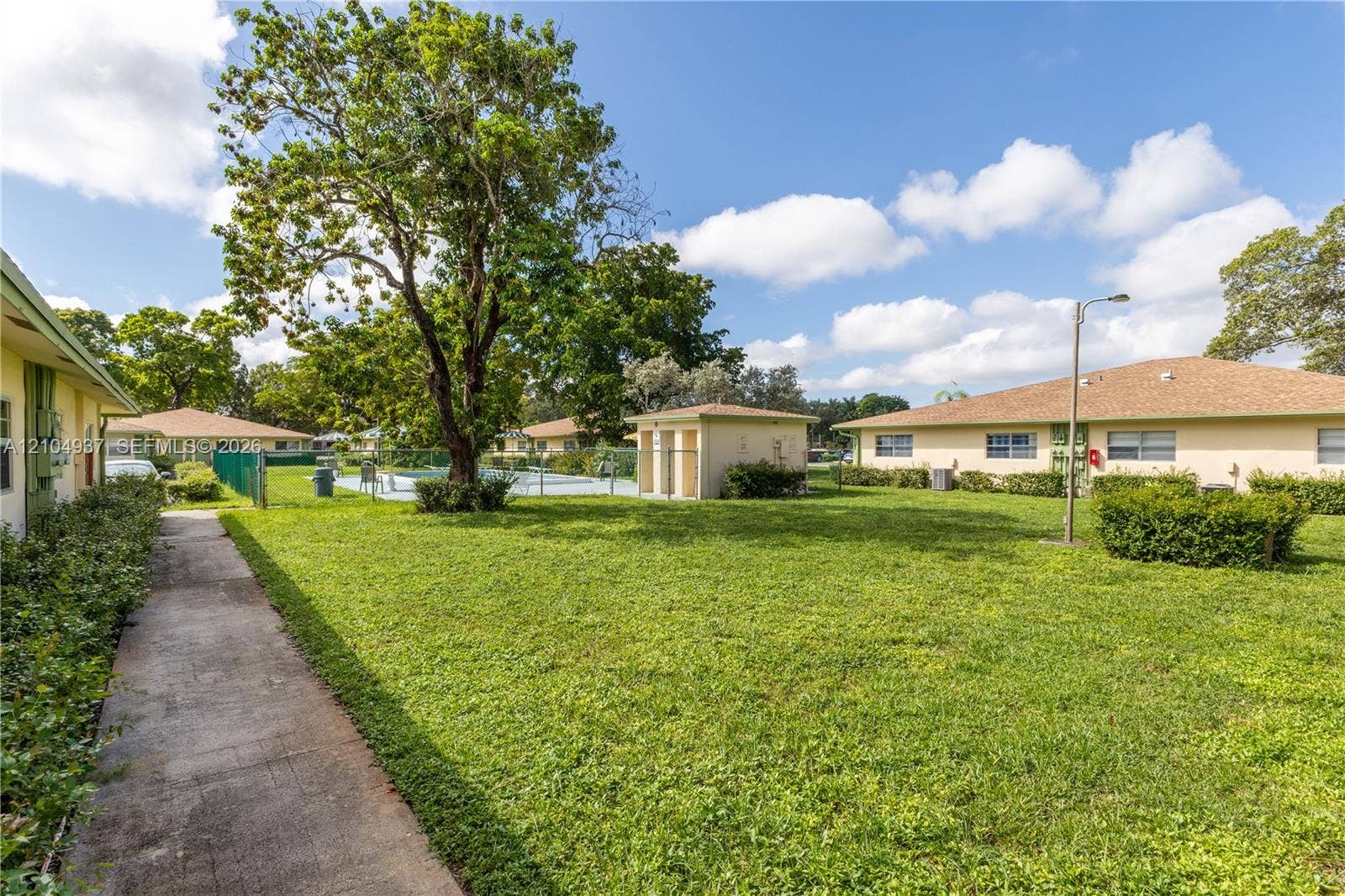 4108 NW 88th Avenue, #3, Coral Springs, FL 33065 Expansive common area featuring a manicured lawn, concrete walkways, mature shade trees, a swimming pool, and an accessory storage structure