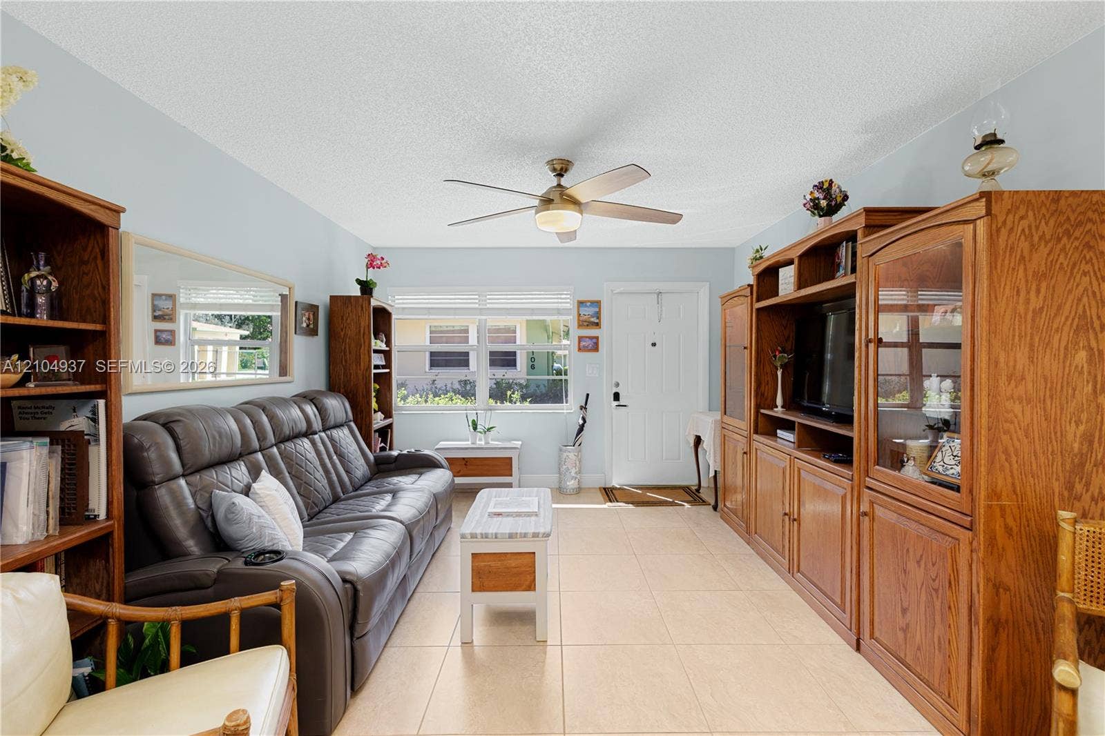 4108 NW 88th Avenue, #3, Coral Springs, FL 33065 Living area featuring large-format tile flooring, a central ceiling fan with integrated lighting, expansive multi-pane windows, and a built-in wooden media cabinet