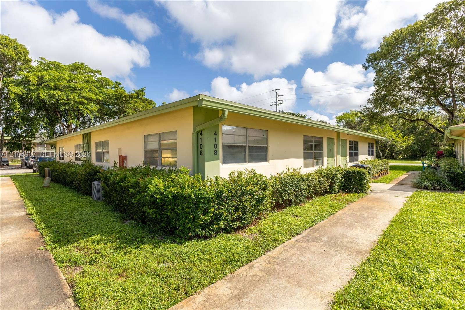 4108 NW 88th Avenue, #3, Coral Springs, FL 33065 Single-story exterior featuring light-toned stucco siding, horizontal sliding windows, a concrete walkway, and manicured perimeter hedges