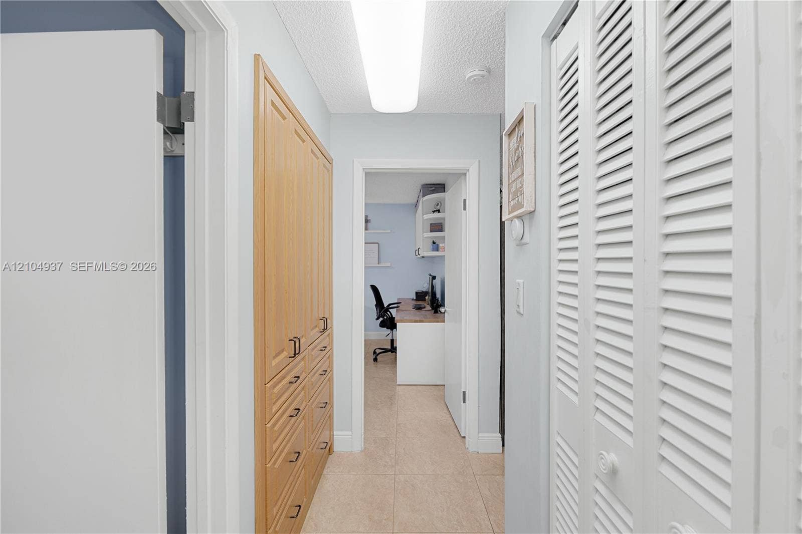 4108 NW 88th Avenue, #3, Coral Springs, FL 33065 Hallway featuring floor-to-ceiling built-in wood cabinetry, white louvered-style closet doors, neutral tile flooring, and linear flush-mount lighting