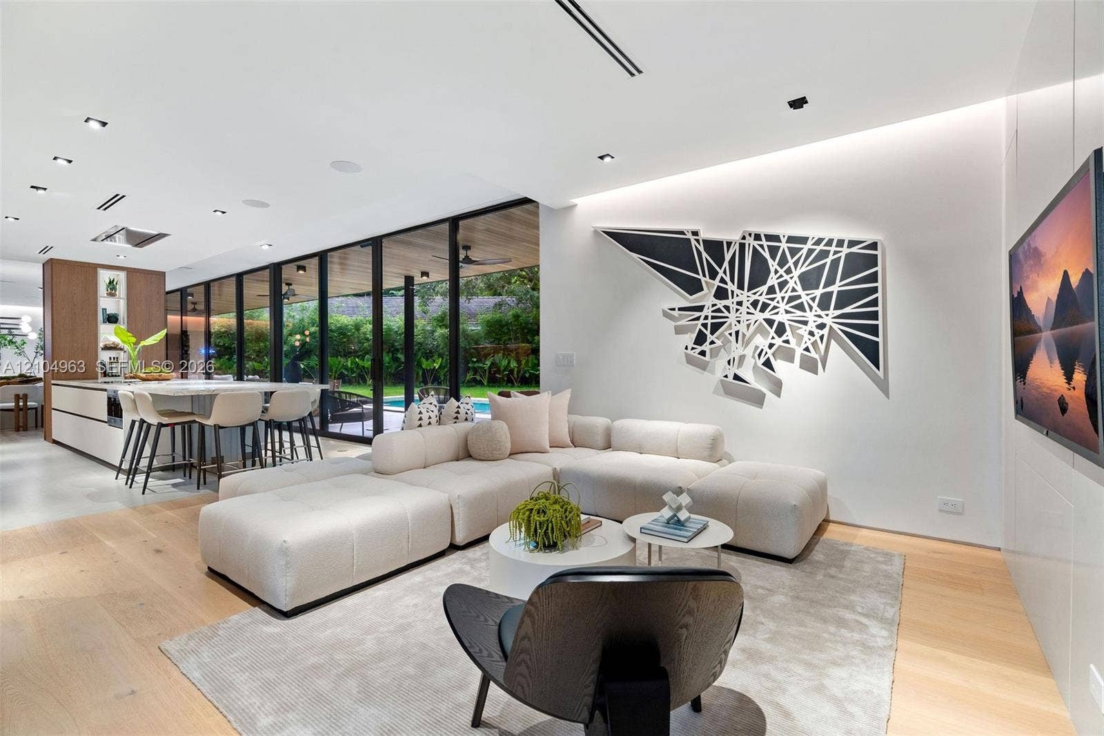 Open-concept floor plan featuring expansive floor-to-ceiling glass panel walls, wood-finish flooring, recessed lighting, and a modern kitchen island with integrated cabinetry