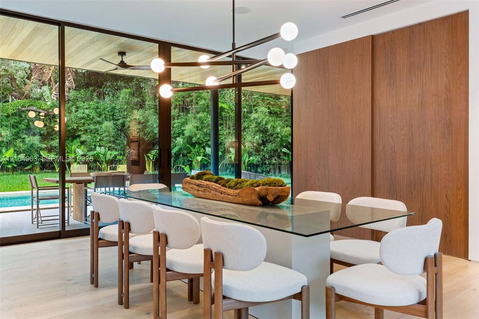 Floor-to-ceiling glass walls, wood-finish wall paneling, modern multi-arm chandelier, wood-finish ceiling, and light-toned wood-finish flooring