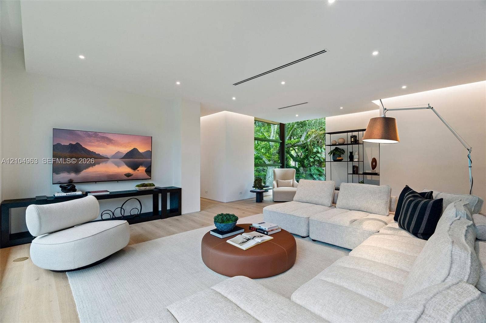 Wide-plank wood-finish flooring, recessed ceiling lighting, linear slot diffusers, and floor-to-ceiling windows featuring exterior greenery