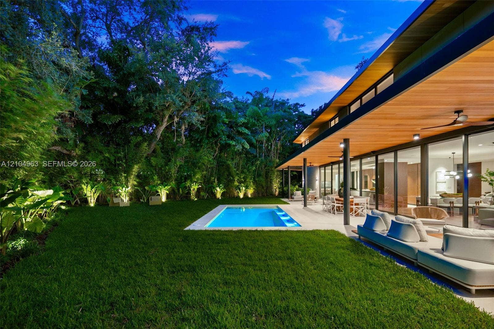 Rear exterior featuring a covered patio with wood-paneled ceiling, sliding glass wall panels, in-ground pool, and manicured lawn