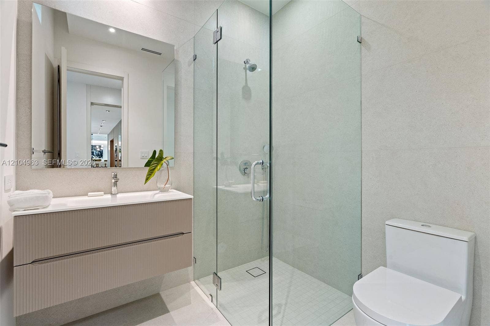Floating vanity with integrated sink, walk-in shower featuring frameless glass enclosure, polished chrome hardware, and large-format wall tiling