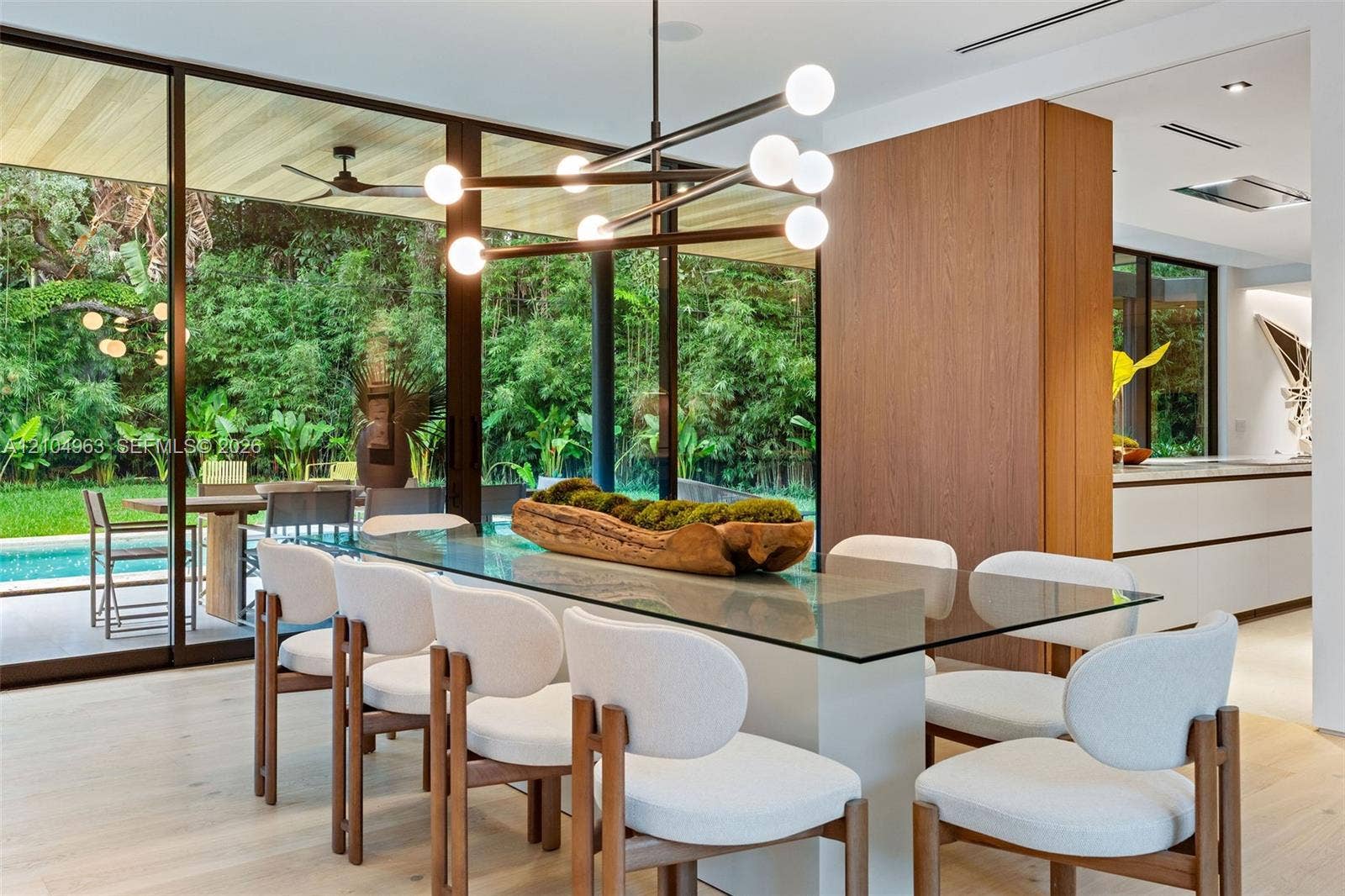Floor-to-ceiling glass walls, wood-finish flooring, architectural multi-bulb chandelier, and wood-paneled feature wall