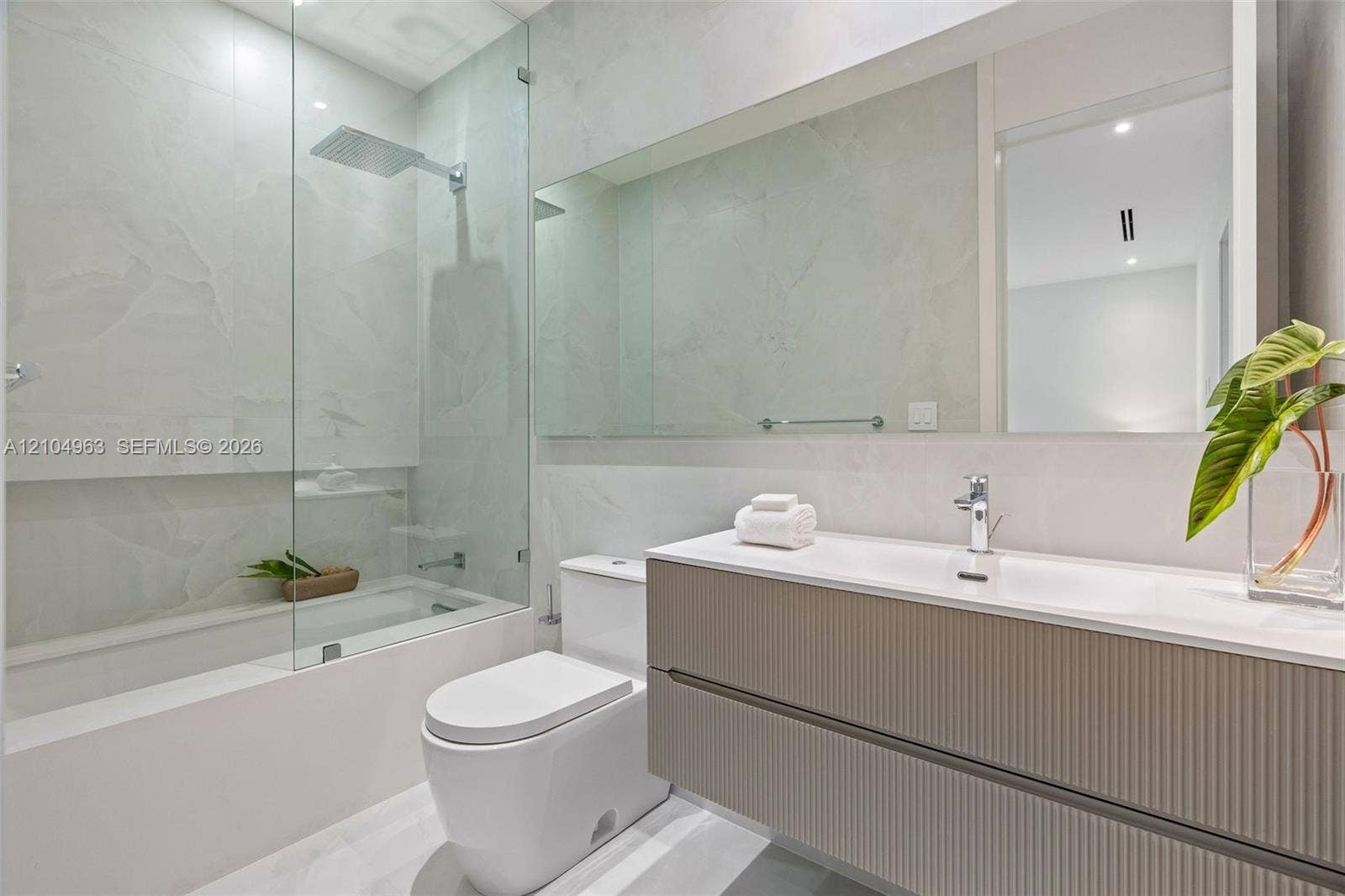 Floating vanity with ribbed cabinetry and integrated sink, frameless glass shower enclosure, rainfall showerhead, large wall-spanning mirror, and neutral-toned wall tiling