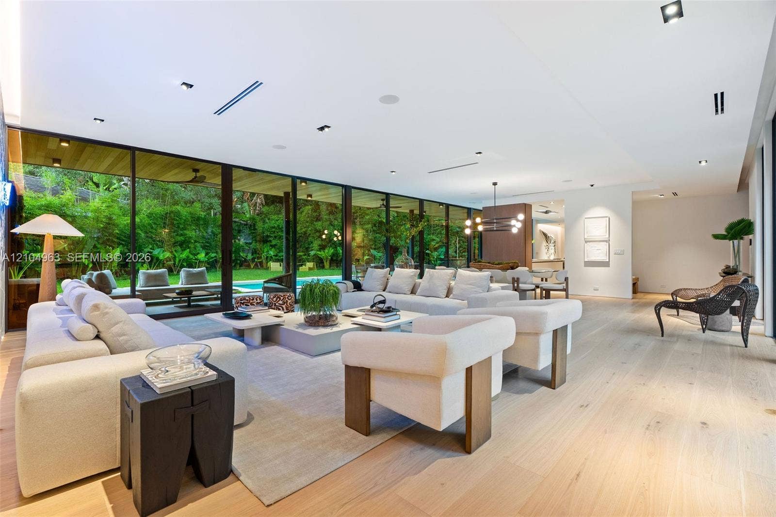 Open-concept interior featuring floor-to-ceiling glass walls, light-toned wood-finish flooring, recessed ceiling lighting, and custom linear architectural fixtures