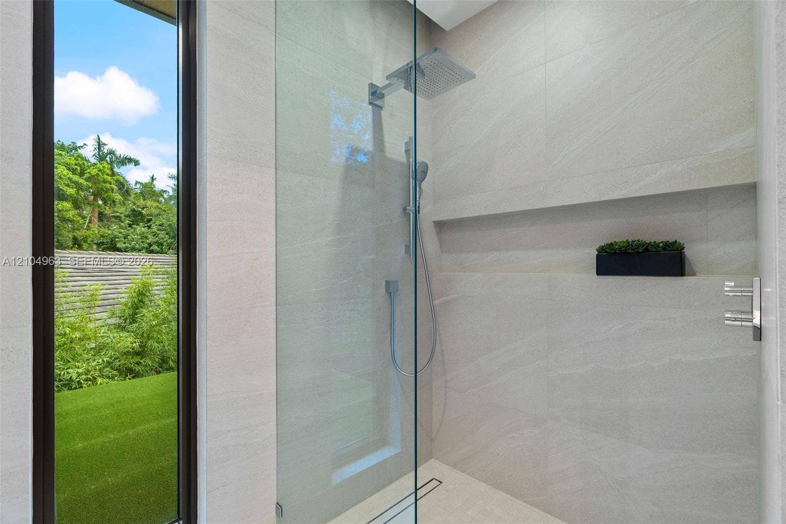 Walk-in shower featuring floor-to-ceiling stone-finish tile, frameless glass enclosure, rainfall shower head, handheld sprayer, and an integrated recessed storage niche