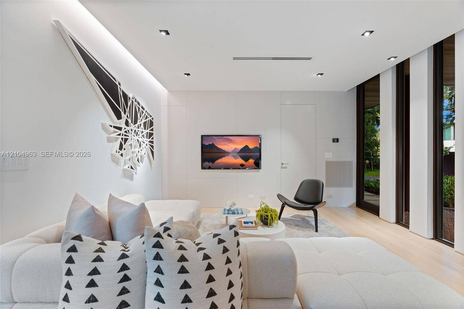 Contemporary interior featuring smooth wall panels, light-toned wood-finish flooring, recessed ceiling lighting, and floor-to-ceiling windows with dark frames