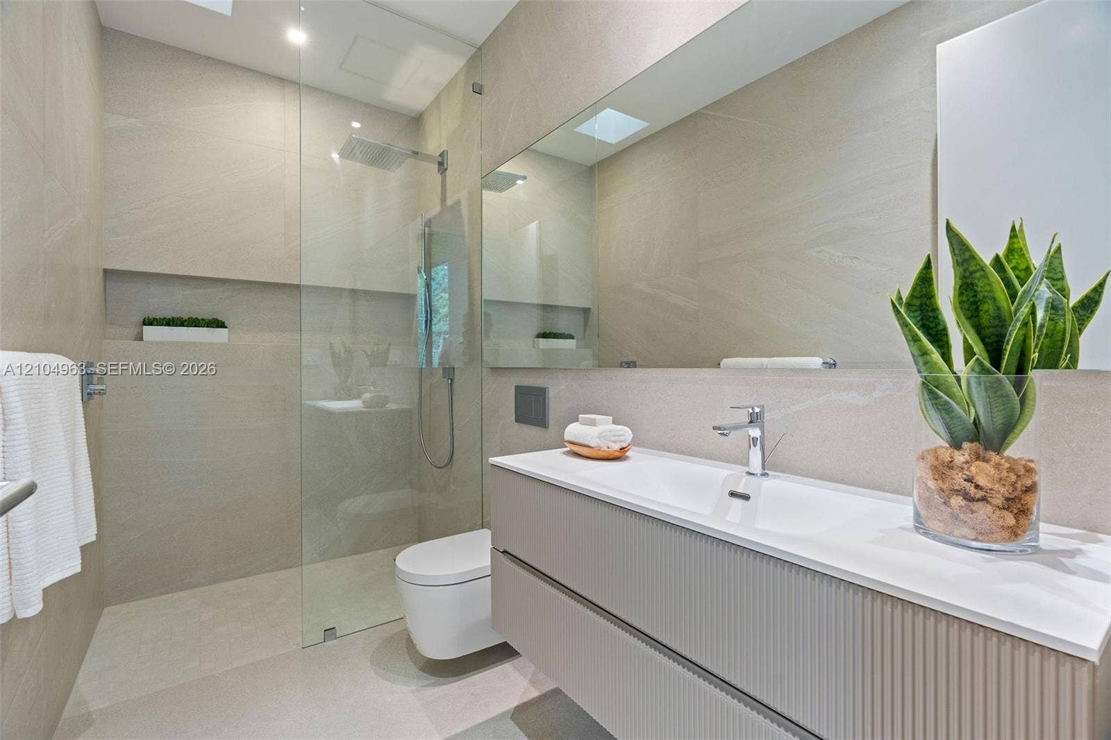Modern bathroom featuring a textured floating vanity, integrated rectangular sink, wall-to-wall mirror, glass-enclosed walk-in shower with a rain-style showerhead, and neutral-toned wall tiles