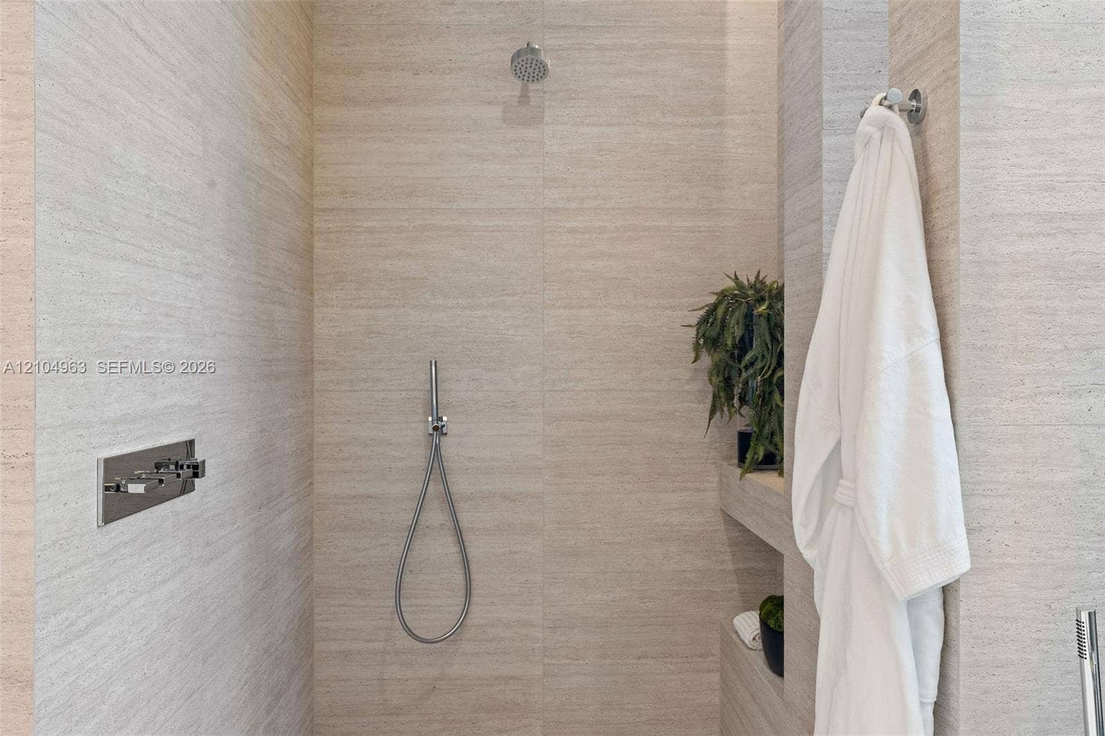 Walk-in shower featuring large-format textured stone wall tile, built-in shelving, a rainfall showerhead, and a wall-mounted handheld shower fixture with chrome hardware